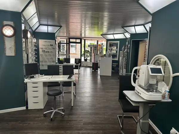 Modernes Optiker-Geschäft mit Brillengestellen, Beratungstisch und Sehtestgerät.